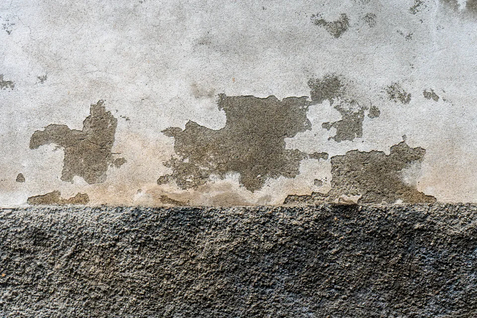 Bas de mur présentant des traces d'humidité et un enduit dégradé